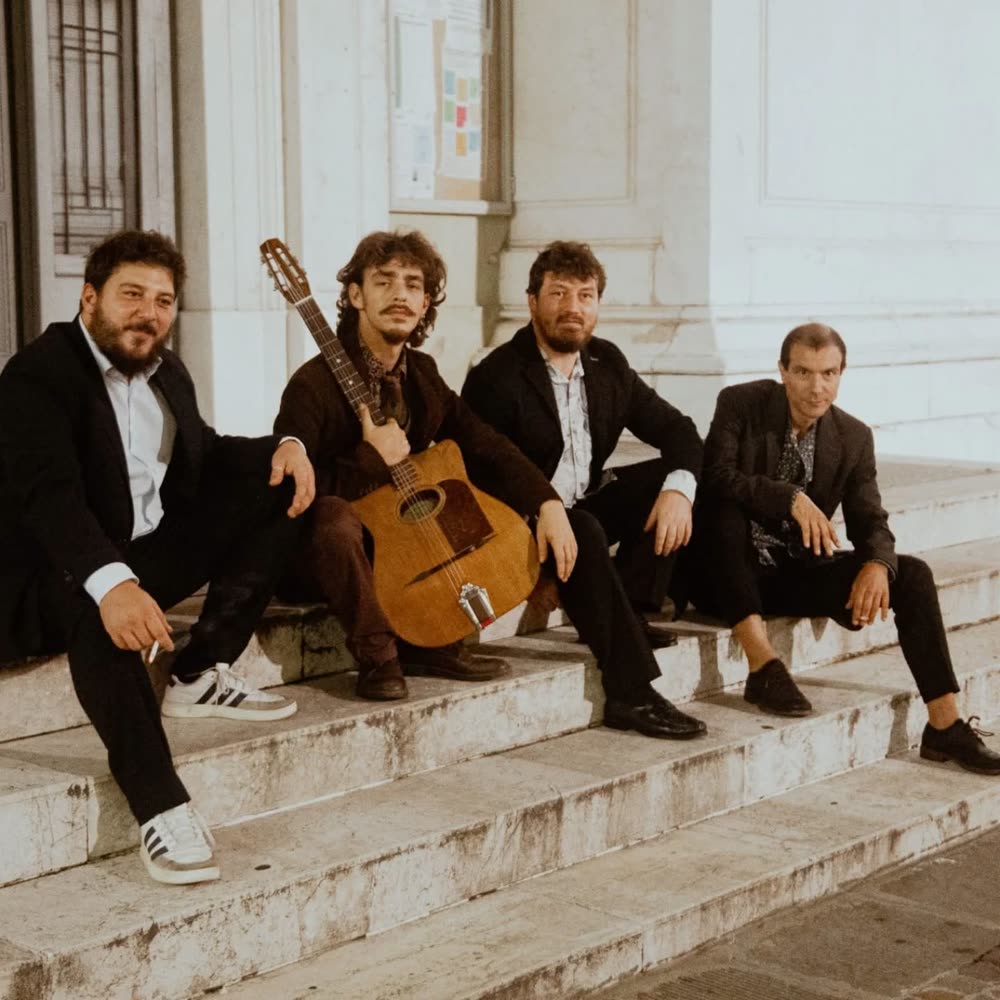I quattro musicisti seduti sui gradini di un edificio, uno con la chitarra manouche in mano
